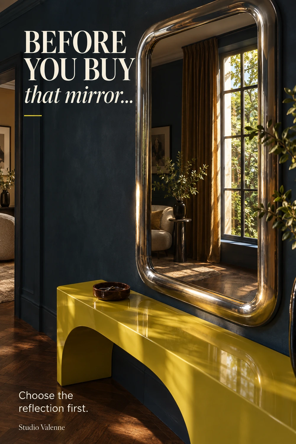 A polished metal mirror above a chartreuse lacquer console in a dark blue entryway reflects a tall sunlit window, golden curtains and a corner of the adjoining room. Ivory text reads Before you buy that mirror… Choose the reflection first.