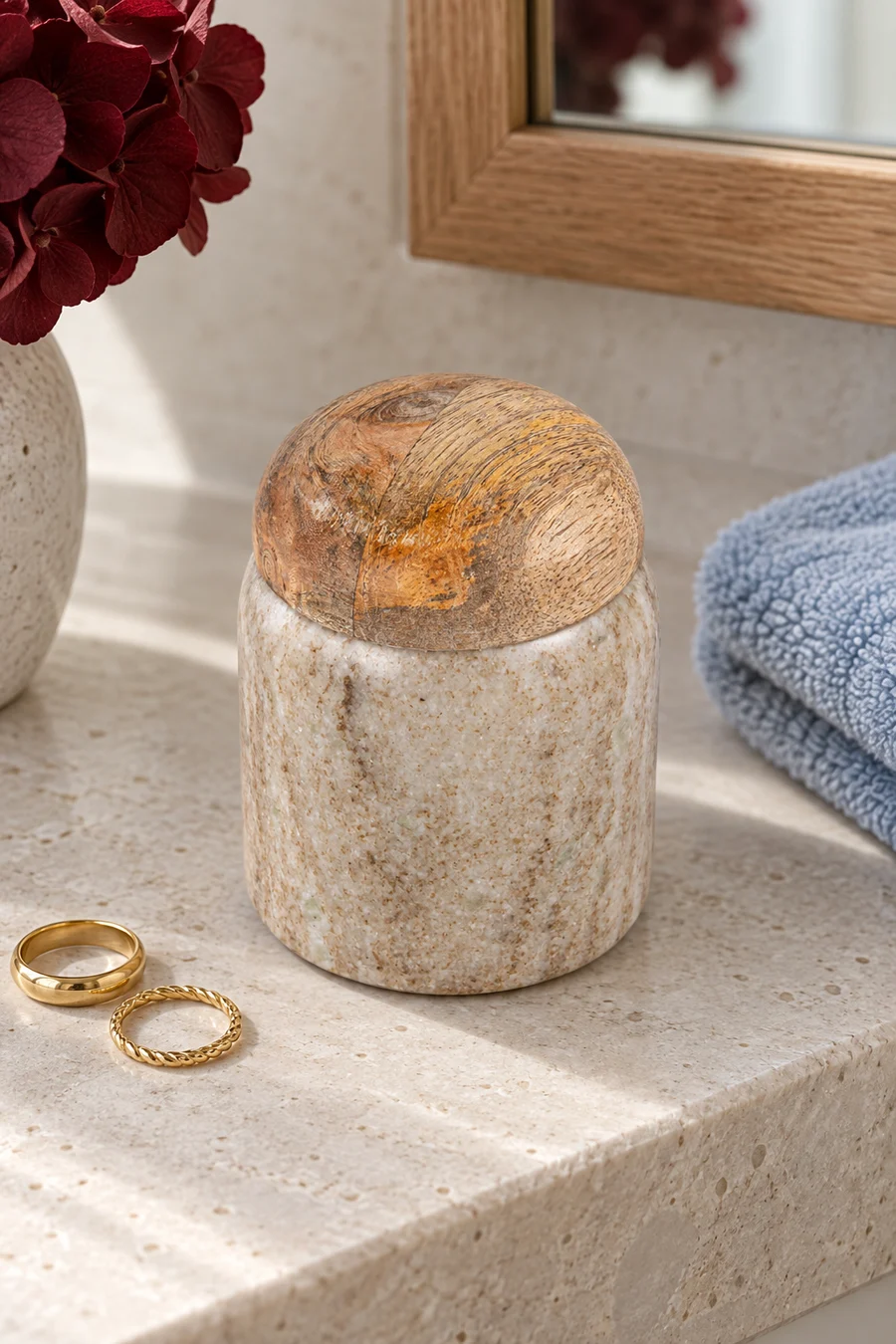 A miniature marble canister with a wood lid beside rings on a stone vanity.