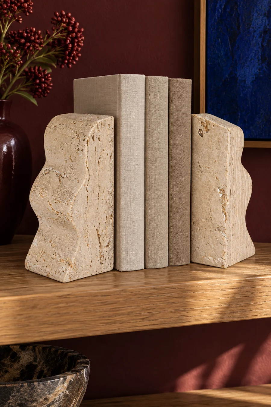 A pair of travertine wave bookends holding books on a wooden console.