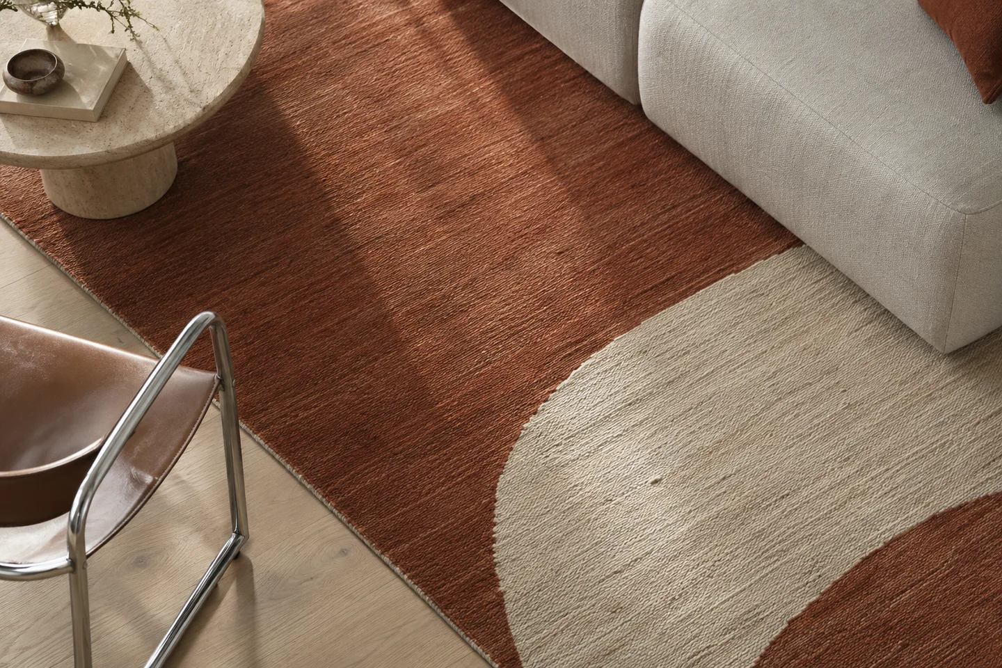 Overhead detail of a rust and cream rug connecting a pale sofa, stone table and chrome chair.